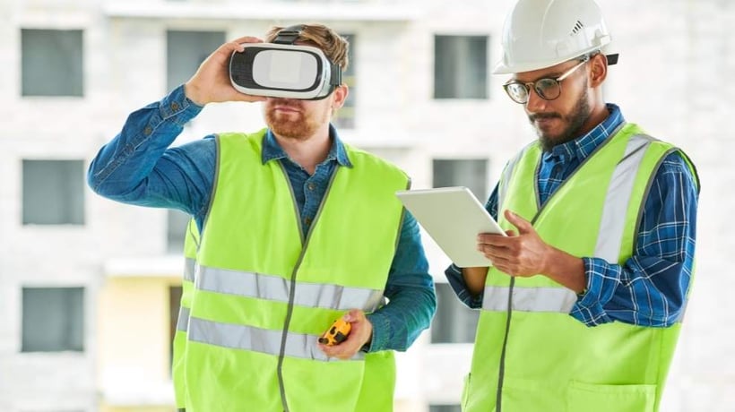 two construction workers in high vis jackets using a virtual reality headset to view a digital twin